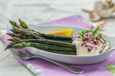 Asparagus oin a bowl topped with white sauce and red onion