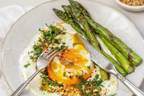 Cooked asparagus and seasoned egg on a plate with a knife and fork on it