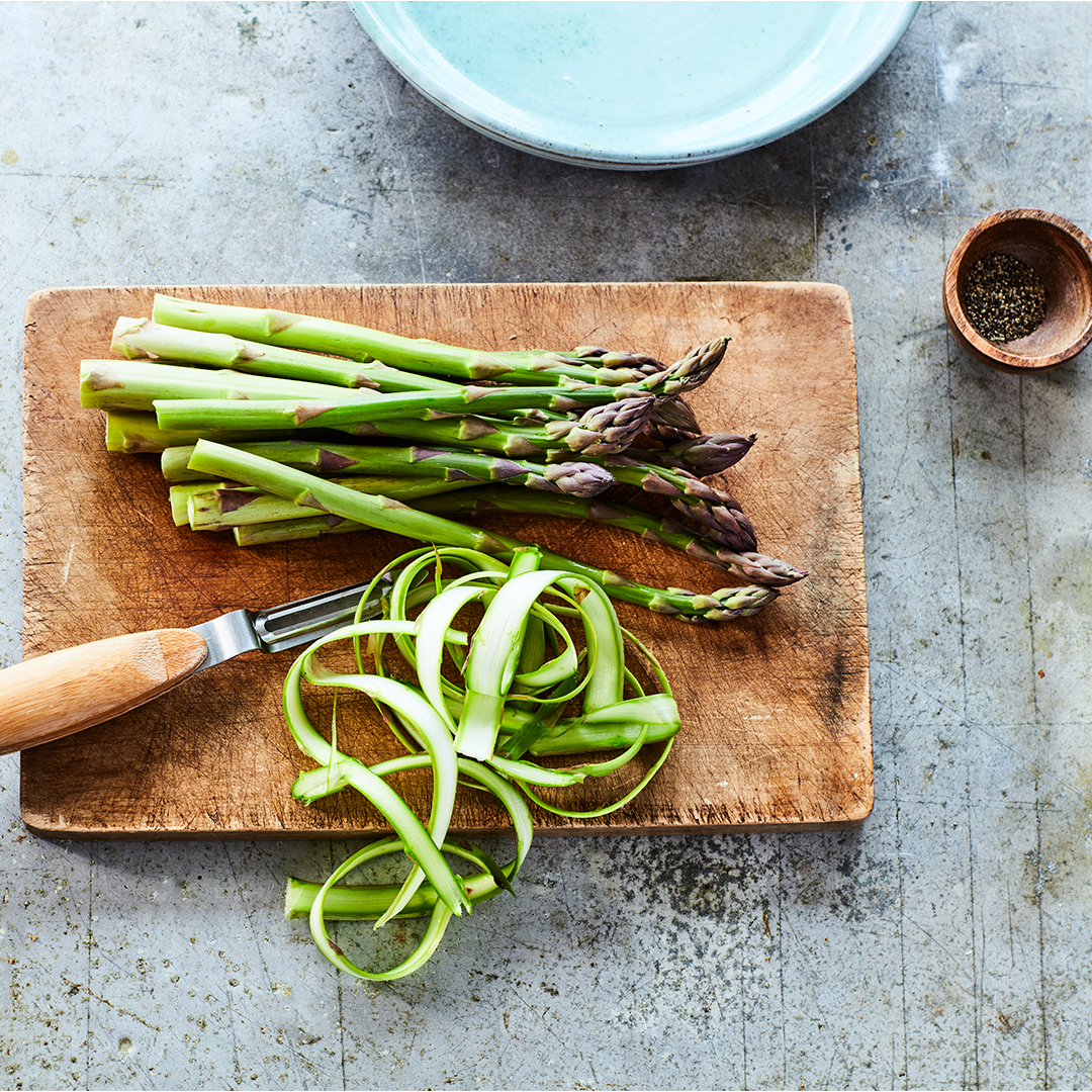 Asparagus bundle next asparagus ribbons below it, on a wooden cutting board